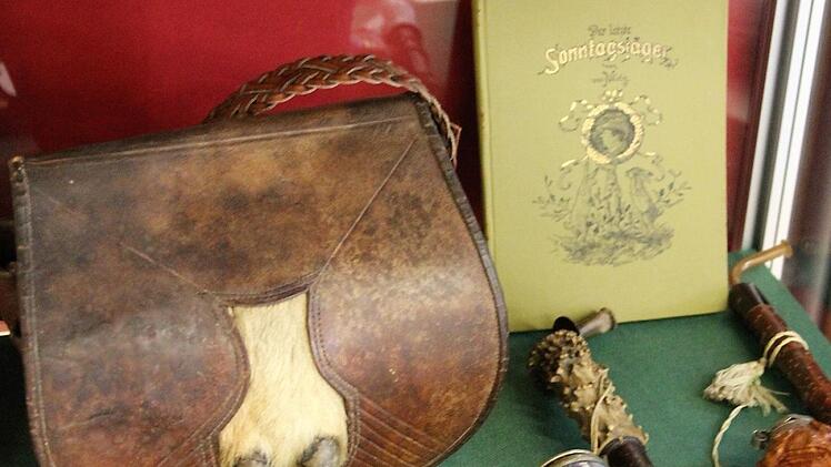 Eine historische Jagdtasche (Ende des 19. Jahrhunderts) liegt neben einem antiken Fernglas und reich verzierten Jäger-Pfeifen. Fuchs