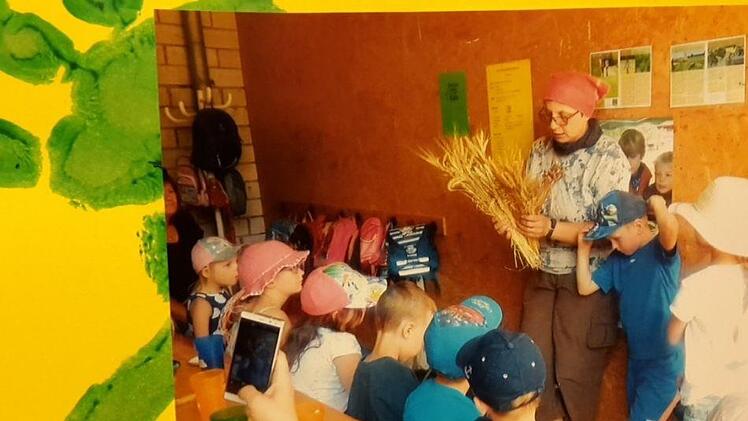 Auf einem Plakat ist Rosi Kuhn zu sehen, wie sie eine Kindergruppe über den Hof führt. Reoro Heike Beudert