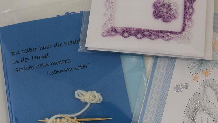 Eine Künstlerin verziert Karten mit Fadenbildern, Häkeleien und Strickereien. Solche Karten sind ein individuelles Geschenk.