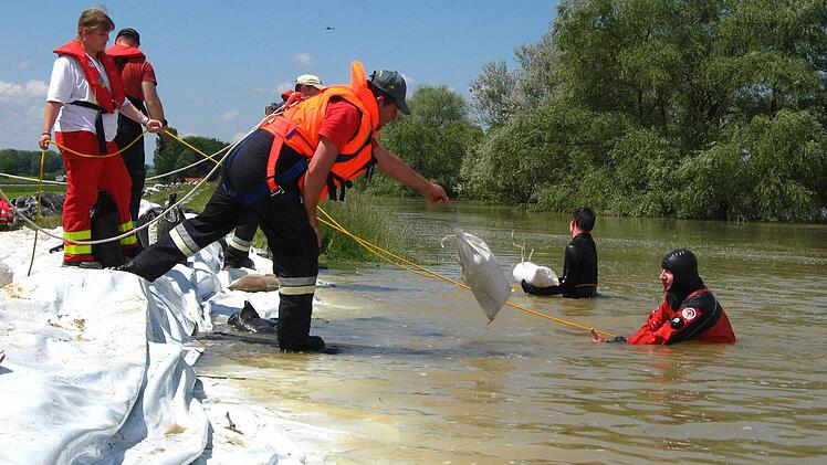 Deichsicherung mit einem Deichsegel (Plane) und Sandsäcken durch Taucher und Wasserretter.