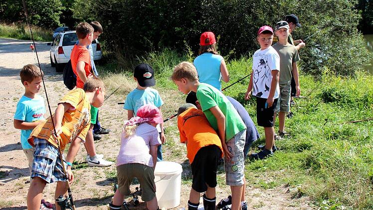 Die Kinder beobachten einen im Eimer zappelnden Fisch.