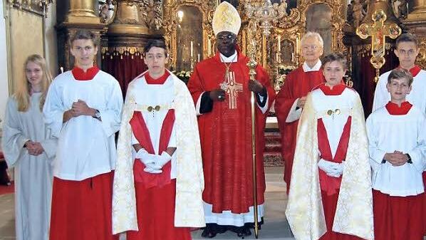 Bischof Sabino Ocan Odoki mit Pfarrer Hans-Werner Alt (beide in der Mitte) und Ministranten vor dem Hauptaltar der Stiftskirche