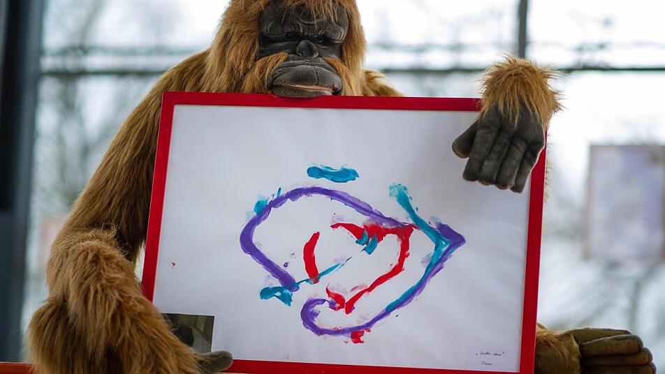 Ein Orang-Utan-Plüschtier ist in Heidelberg im Zoo mit einem von Menschenaffen gemalten Bild zu sehen. Der Heidelberger Zoo versteigerte im Rahmen einer Auktion Kunstwerke, die von Menschenaffen und Elefanten geschaffen wurden. Foto: Uwe Anspach/dpa