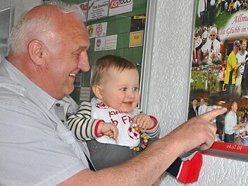 Georg "Bobby" Distler zeigt seinem Enkel Mats, der natürlich einen Club-Latz um den Hals trägt, die Erinnerungscollage vom Gastspiel des FCN in Effeltrich. Anscheinend hat der Hosenmatz den Opa auf dem Bild erkannt.