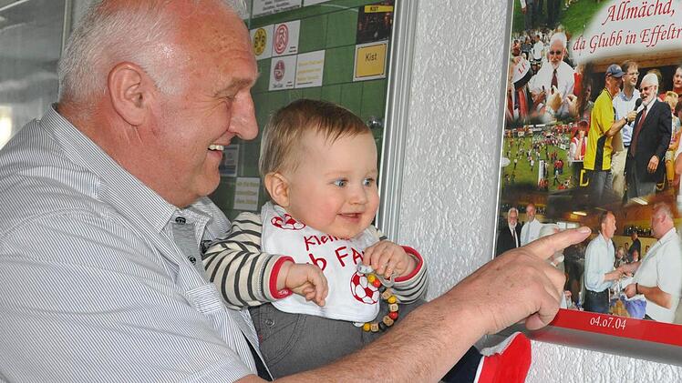 Georg "Bobby" Distler zeigt seinem Enkel Mats, der natürlich einen Club-Latz um den Hals trägt, die Erinnerungscollage vom Gastspiel des FCN in Effeltrich. Anscheinend hat der Hosenmatz den Opa auf dem Bild erkannt.