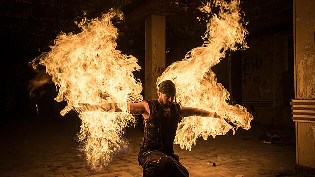 Ein Künstler mit Flammen in den Händen schafft eine beeindruckende Feuershow. Die dynamischen Bewegungen in einer düsteren Umgebung lassen auf eine magische Darbietung schließen.