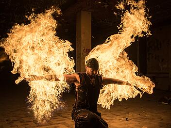Ein Künstler mit Flammen in den Händen schafft eine beeindruckende Feuershow. Die dynamischen Bewegungen in einer düsteren Umgebung lassen auf eine magische Darbietung schließen.