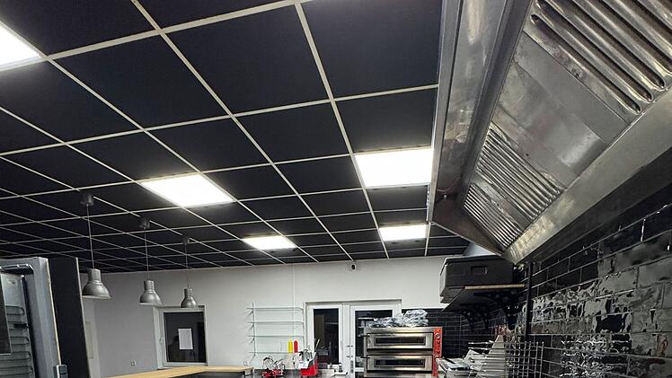 Gewerbliche Küche in Oberhaid mit moderner Ausstattung: Edelstahl-Arbeitsflächen, Öfen und Kochfelder. Helle Beleuchtung und aufgeräumtes Design. Vorbereitung für eine Pizzeria-Eröffnung.