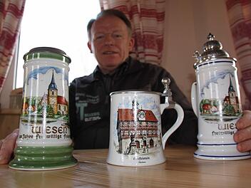 Franz Böhmer mit drei Bierkrügen, die heimatliche Motive aus Bad Staffelstein und seinem Heimatdorf Wiesen zeigen. Foto: Matthias Einwag