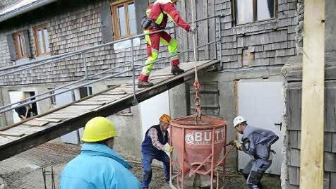 Schwieriges Manövrieren: Am Betonkübel hängt ein Hubschrauber (nicht im Bild), drunter dirigiert einer Piloten, Heinz Pfeffer, Heinz Steidle und Rainer Hänelt (von links) laden den Beton ab.