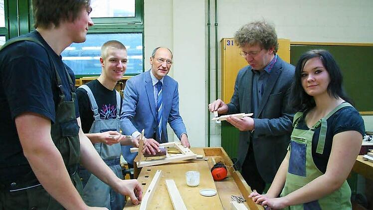 Johannes Kabilka, Patrick Spiegel und Jennifer Roberts zeigen Bruno Buchen und Frank Ackermann, wie sie eine Stuhllehne bauen. Da packen der Schulleiter und der Obermeister der Schreinerinnung Kitzingen gleich mit an. Foto: Sabine Paulus