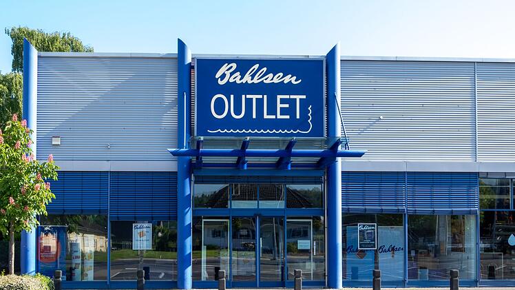Das Bild zeigt das Bahlsen Outlet, ein Geschäft mit großer blauer Beschilderung. Es gibt Parkplätze davor und es ist ein moderner, funktionaler Bau.
