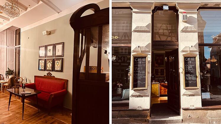 Ein stilvoll eingerichtetes Caf&eacute; mit rotem Sofa und Kunstwerken an der Wand. Drau&szlig;en zwei Schilder mit der Aufschrift "Caf&eacute;" und einer einladenden offenen T&uuml;r.