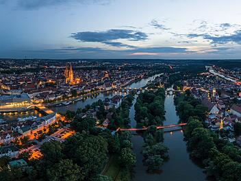 Panorama der Stadt Regensburg in Bayern mit dem Fluss Donau dem beleuchtetem Dom und der steinernen Brücke im Sommer zur blauen Stunde im Zwielicht, Deutschland