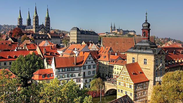 Historische Altstadt mit Fachwerkh&auml;usern und einem Fluss. Im Hintergrund sind alte Geb&auml;ude und Kirchen sichtbar, die Bambergs reiche Geschichte und Kultur widerspiegeln.