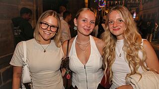 Endlich wieder Sandkerwa! Drei junge Frauen lächeln in die Kamera bei der Bamberger Sandkerwa 2026. Die Straße ist belebt und festlich beleuchtet.