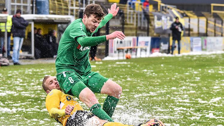 Auf dem schneebedeckten Rasen im Stadion Gr&uuml;ne Au war das Fu&szlig;ballspielen nur bedingt m&ouml;glich. Hier verliert der Sander Max Witchen (gr&uuml;nes Trikot) den Ball gegen den Hofer Matej Kyndl. Foto: Ryan Evans