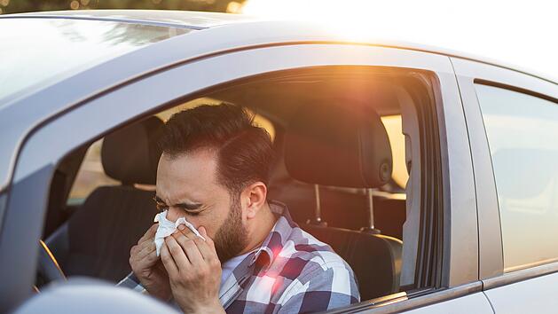Gesundheit, Virus, Allergie, Taschentuch, Schneuzen . Young man sneezing while driving car. Healthcare, virus, allergy concept.