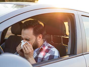 Gesundheit, Virus, Allergie, Taschentuch, Schneuzen . Young man sneezing while driving car. Healthcare, virus, allergy concept.