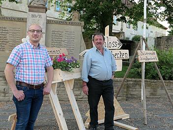 Mit-Organisator des Ebenhäuser Pfingstmärktle, Fabian  Wahler (links) präsentiert die neuen von Hobby-Holzwurm Ludwig Hilpert  (rechts) gefertigten Wegweiser und Willkommensschilder vor der Kulisse  des alten Schlosses mit dem Kriegerdenkmal. Foto: Elisabeth Mehn