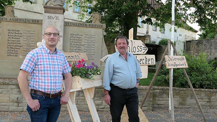 Mit-Organisator des Ebenhäuser Pfingstmärktle, Fabian  Wahler (links) präsentiert die neuen von Hobby-Holzwurm Ludwig Hilpert  (rechts) gefertigten Wegweiser und Willkommensschilder vor der Kulisse  des alten Schlosses mit dem Kriegerdenkmal. Foto: Elisabeth Mehn