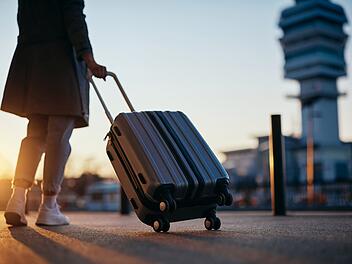 Nahaufnahme einer Reisenden mit ihrem Gepäck, die bei Sonnenuntergang am Flughafen ankommt. Close up of woman with suitcase at airport at sunset. Copy space. Koffer, Gepäck