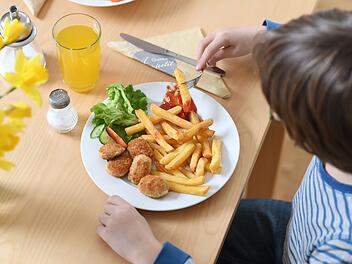 Ein Kind isst Chicken Nuggets und Pommes Frites