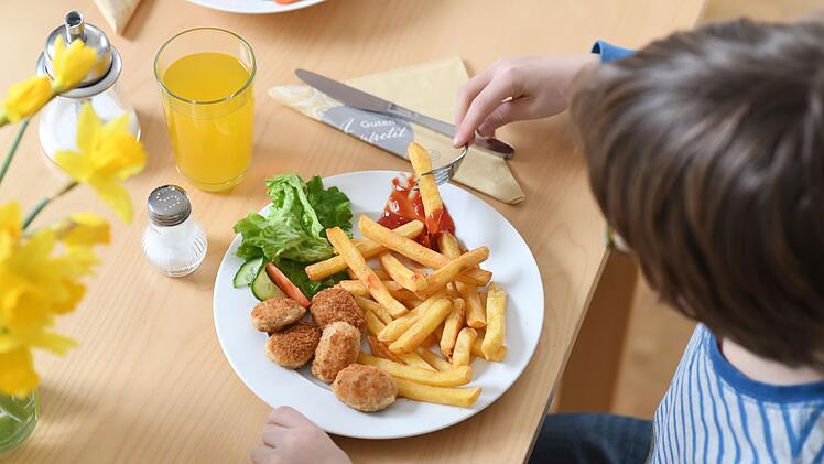 Ein Kind isst Chicken Nuggets und Pommes Frites