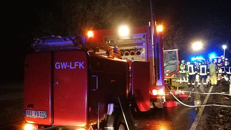 Sachsen-Anhalt, K&ouml;then: Feuerwehrleute und Rettungskr&auml;fte stehen auf einer Landstra&szlig;e hinter einem ausgebrannten Auto. Bei dem Autounfall sind drei Menschen, darunter ein Kind, verbrannt. Ein S&auml;ugling wurde aus dem Wrack gerettet. Foto: Heiko Rebsch/dpa-Zentralbild/dpa