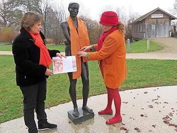 Monica Schütz (links) und Barbara von Mengershausen dekorieren die orangefarbenen Schals an den Skulpturen im Bad Staffelsteiner Kurpark. Foto: Monika Schütz