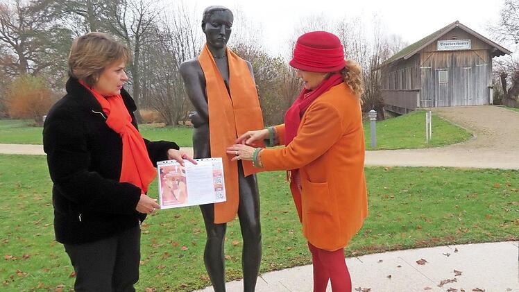 Monica Schütz (links) und Barbara von Mengershausen dekorieren die orangefarbenen Schals an den Skulpturen im Bad Staffelsteiner Kurpark. Foto: Monika Schütz
