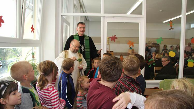Die Hortkinder gingen voraus - und die beiden Pfarrer weihten den Kinderhort: Pfarrer Wolfgang Eßel hatte sich einen grünen Zweig als Symbol für das Leben abgezwickt, mit diesem verspritze er das Weihwasser; und der evangelische Pfarrer Wolfgang Oertel hatte eine Geschichte für die Kinder dabei. Foto: Sonja Adam