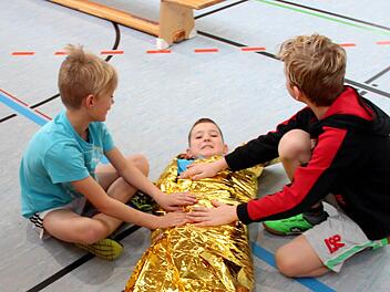 Jonathan in der Rettungsdecke, von Carlos (unten, links ) und Mika ist er fachgerecht eingepackt worden. Fotos: Johanna Blum