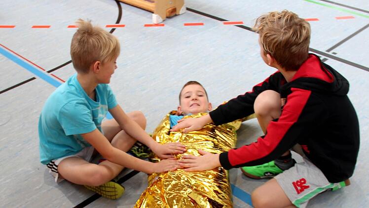 Jonathan in der Rettungsdecke, von Carlos (unten, links ) und Mika ist er fachgerecht eingepackt worden. Fotos: Johanna Blum