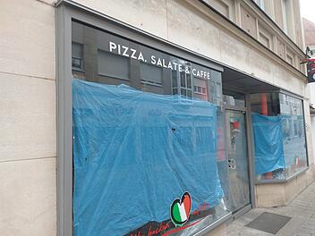 Geschlossenes Restaurant mit blauem Sichtschutz. Schilder zeigen "Pizza, Salate & Caff&egrave;". Abschiedsbotschaft und italienisches Herz-Logo auf dem Fenster.