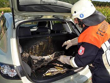 Ein Feuerwehrmann zeigt den Schaden: Der Kofferraum des Unfallwagens ist total verkohlt. Fotos: Peter Rauch