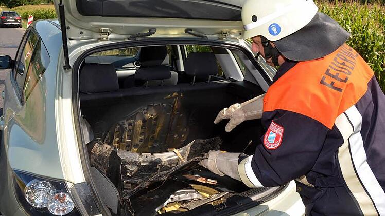 Ein Feuerwehrmann zeigt den Schaden: Der Kofferraum des Unfallwagens ist total verkohlt. Fotos: Peter Rauch