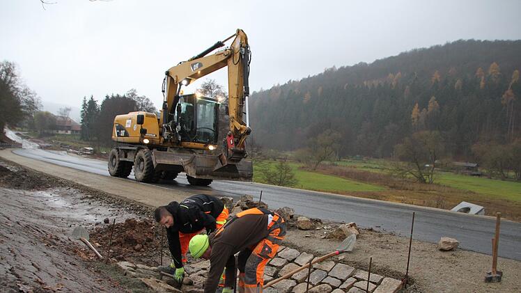 Zwei Bauarbeiter pflastern einen Regenablauf am Rande der neu gebauten Straße. Foto: Ulrike Müller