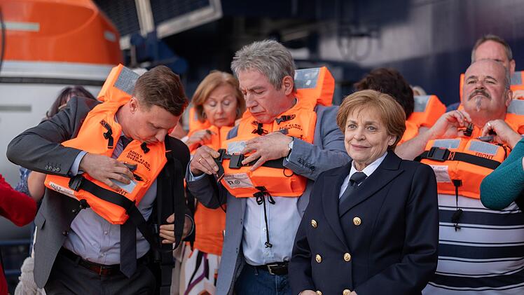 Bodyguard Mike (Tim Kalkhof, links) und Joachim Sauer (Thorsten Merten) machen sich mit den Sicherheitsvorschriften an Bord vertraut. Angela Merkel (Katharina Thalbach) sieht das etwas großzügiger.
