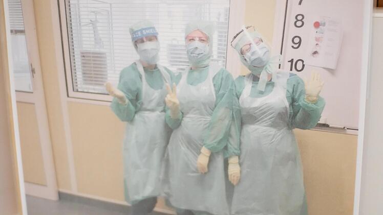 Das Foto zeigt drei Mitarbeiterinnen in Ganzk&ouml;rpermontur. Alle drei l&auml;cheln. Doch unbeschwerte Momente waren auf der Intensivstation Anfang 2021 selten.