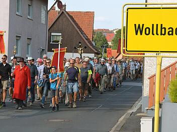 Pilgerführer Klaus Rind - der Herr im roten Mantel - inmitten seiner Wanderer auf seinem Weg durch Wollbach.  Fotos: Peter Rauch