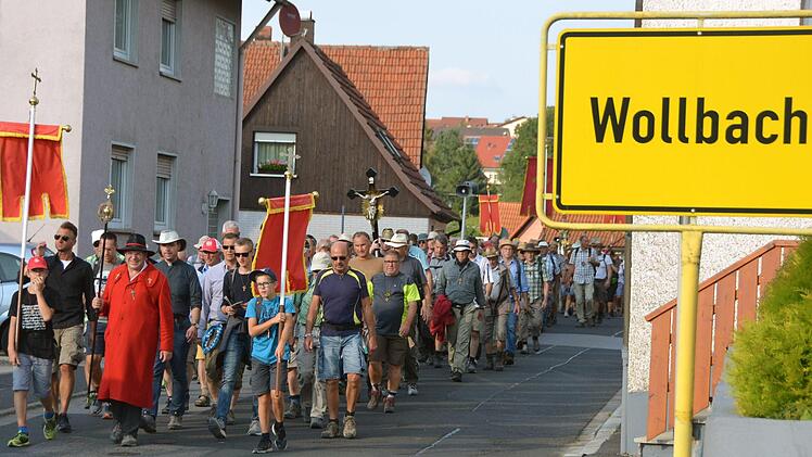 Pilgerführer Klaus Rind - der Herr im roten Mantel - inmitten seiner Wanderer auf seinem Weg durch Wollbach.  Fotos: Peter Rauch
