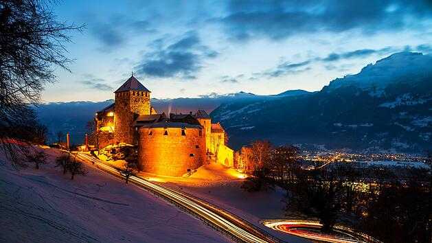 Vaduz, Liechtenstein. Illuminated castle of Vaduz at sunset Vaduz, Liechtenstein. Illuminated castle of Vaduz at sunset - popular landmark at night, with car traffic lights and sunset sky, mountains at the background
