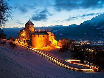 Vaduz, Liechtenstein. Illuminated castle of Vaduz at sunset Vaduz, Liechtenstein. Illuminated castle of Vaduz at sunset - popular landmark at night, with car traffic lights and sunset sky, mountains at the background