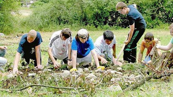 Für ihr Kunstwerk auf einer Wiese neben der Lebenshilfe Haßberge in Sylbach legen sich die Berufsschul-stufenschüler (von rechts: Michelle, Michael, Bastian, Toni, Diana, Karsten und Bobby) ganz schön ins Zeug. Für die Spirale werden Äste, Zweige, Steine, Gräser und Blüten gebraucht. Links ist die Referendarin Elisabeth Freisinger, die die Schüler unterstützt. Am Freitag soll alles fertig sein.  Foto: Ralf Naumann