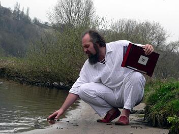 Am Mainufer berührt Heiko Herbert das klare Wasser. Mit Hilfe der Shruti-Box in seiner Hand will er die Menschen mit der Natur verbinden. Fotos: Peter Pfannes