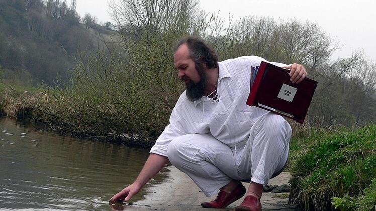 Am Mainufer berührt Heiko Herbert das klare Wasser. Mit Hilfe der Shruti-Box in seiner Hand will er die Menschen mit der Natur verbinden. Fotos: Peter Pfannes