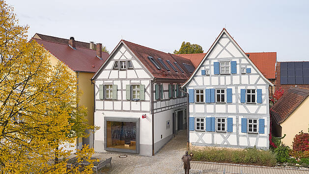 Das Bild zeigt ein Fachwerkhaus mit blauen Fensterl&auml;den, das Levi Strauss' Geburtshaus in Buttenheim ist. Es dient als Museum &uuml;ber Jeansgeschichte. Eine Statue steht im Hof.