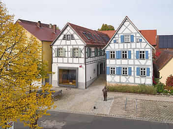 Das Bild zeigt ein Fachwerkhaus mit blauen Fensterl&auml;den, das Levi Strauss' Geburtshaus in Buttenheim ist. Es dient als Museum &uuml;ber Jeansgeschichte. Eine Statue steht im Hof.