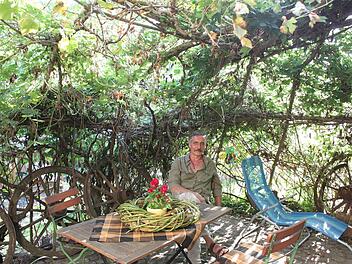 Ganz von schützendem Grün umgeben: Heinrich Geßlein sitzt in seinem Lieblingsflechtobjekt vor seinem Haus in Marktgraitz. Aus Weide geformt wie diese Pergola ist auch der Tischschmuck, ein grüner Kranz mit Blumenstock in der Mitte. Fotos: Ramona Popp